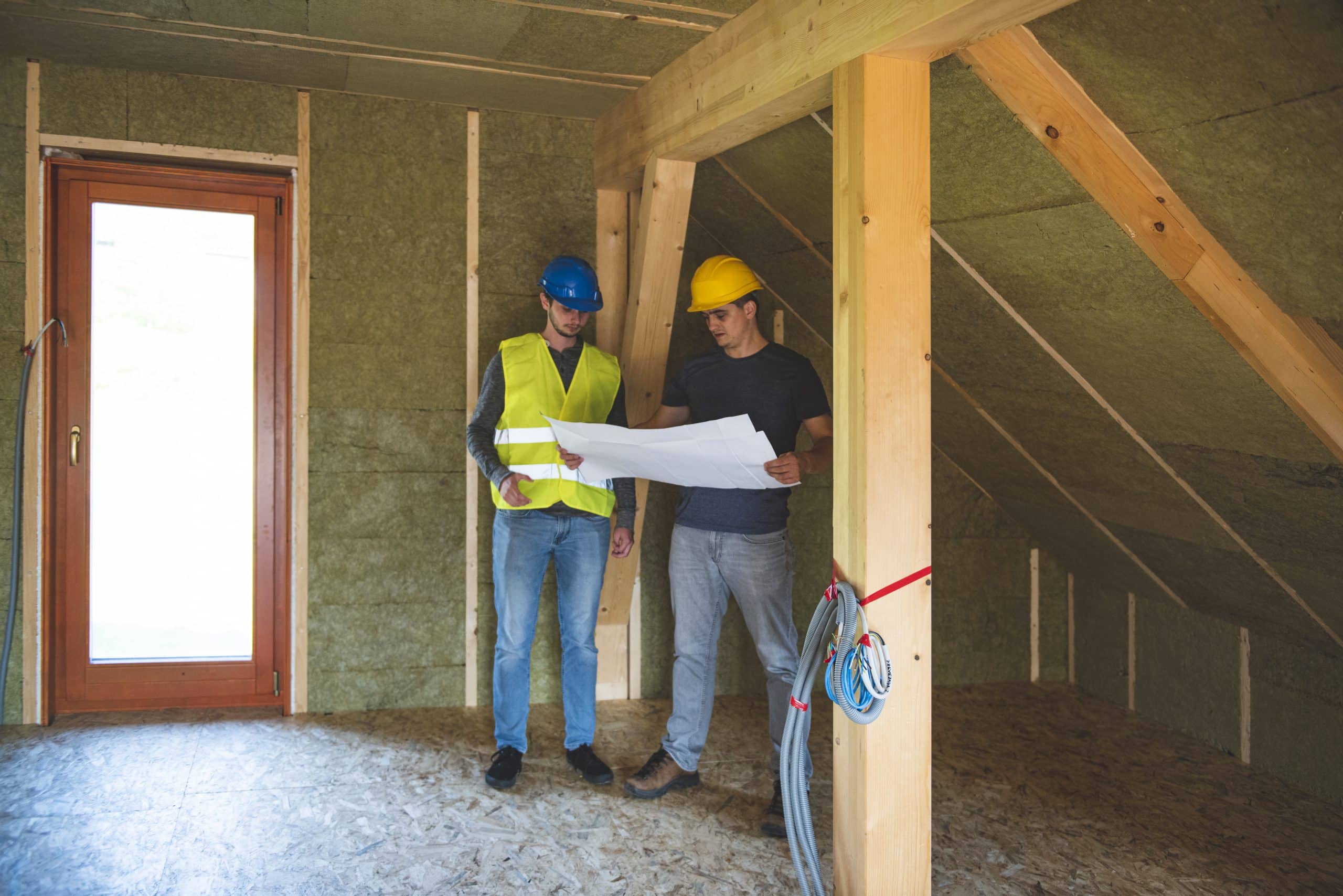 Construction workers reviewing blueprint at construction site.Roof with mineral rockwool in wall section. House under construction with insulation glass wool on an attic floor