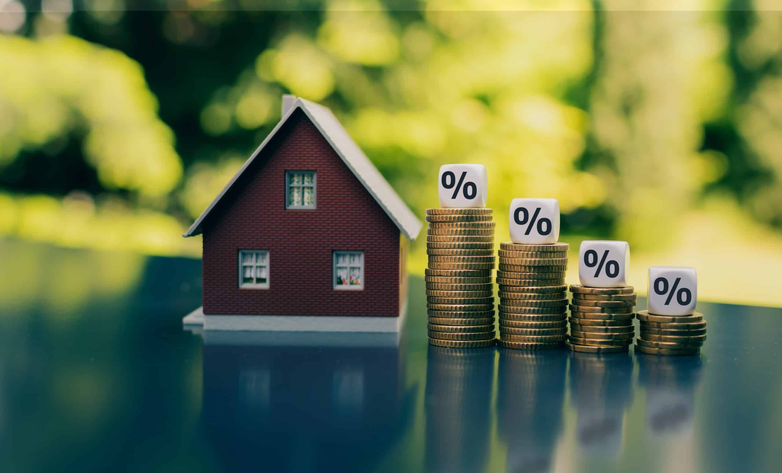 Symbol for decreasing interest rates. Dice with percentage symbols on decreasing high stacks of coins next to a model house.