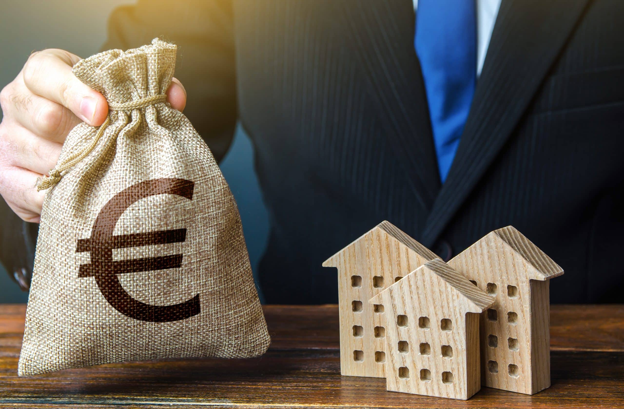 Euro money bags and residential buildings figures. Investments in real estate and construction industry. Taxes. Bank offer of mortgage loan. Rental business. Sale of housing. Buy. Municipal budget.