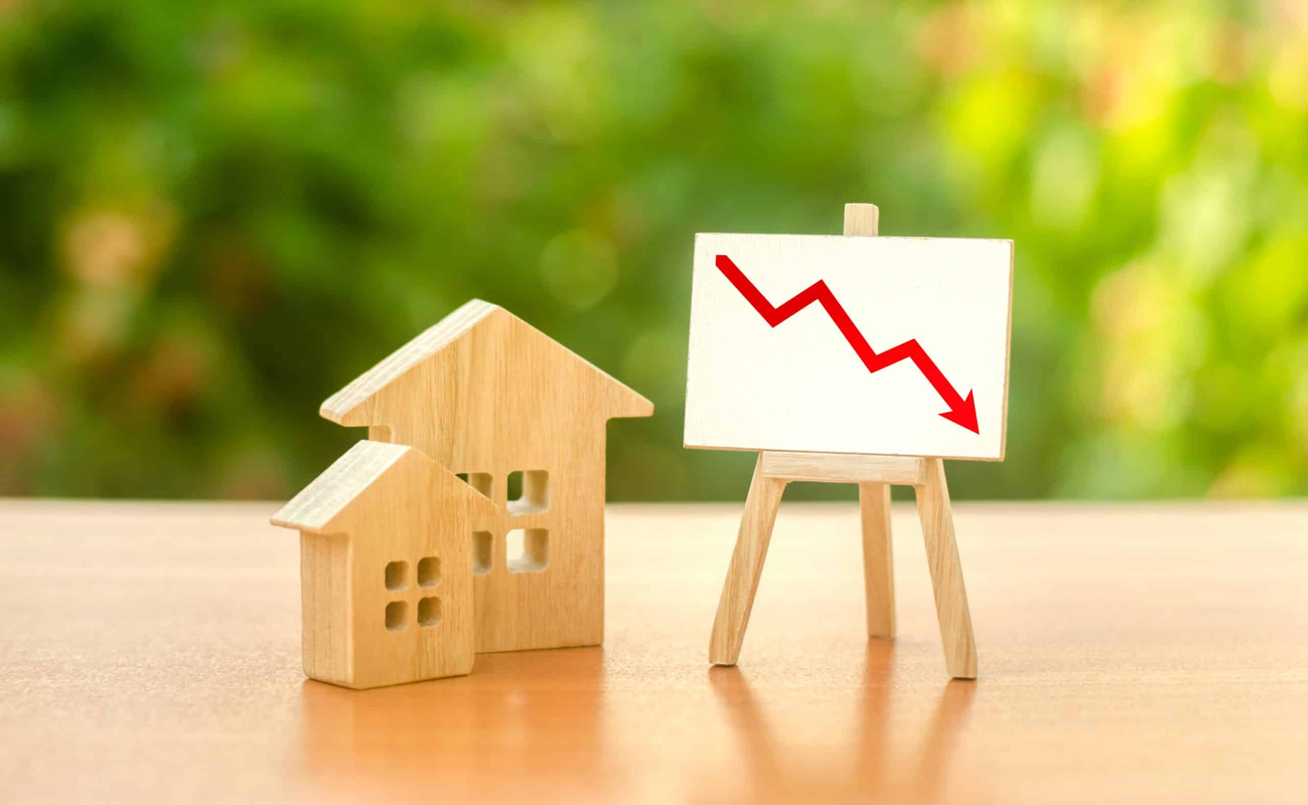 Wooden houses and an easel red arrow down. The fall of the real estate market. concept of value or cost decrease. low liquidity and attractiveness. cheap rent. Reduced demand and stagnation.