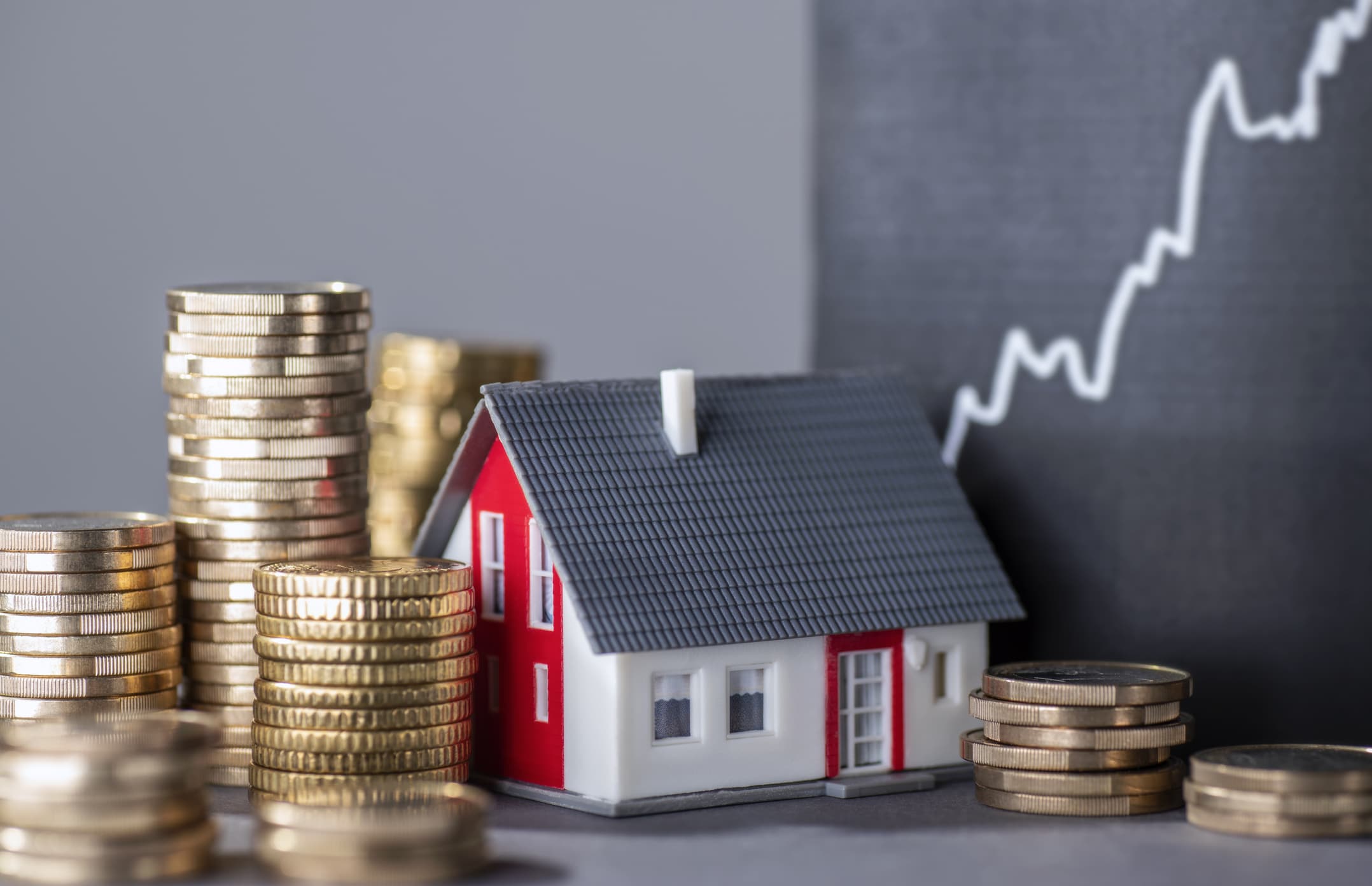 House with stacks of money and a rising curve symbolizing rising real estate prices