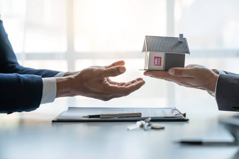 Young Asian real estate agent, and insurance salesman handing over a sample house to a client after signing the sale at the office.