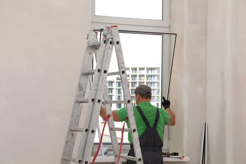 Worker in uniform installing double glazing window indoors, back view